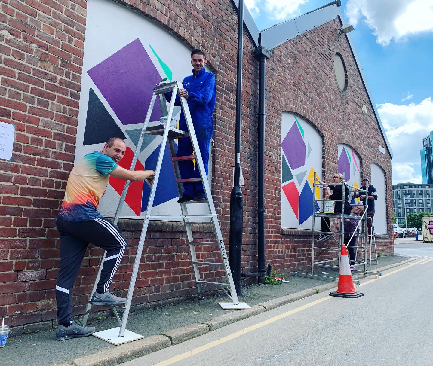Two people working on an ArtWorks South Yorkshire project, both stood on a ladder outside a building by the piece.
