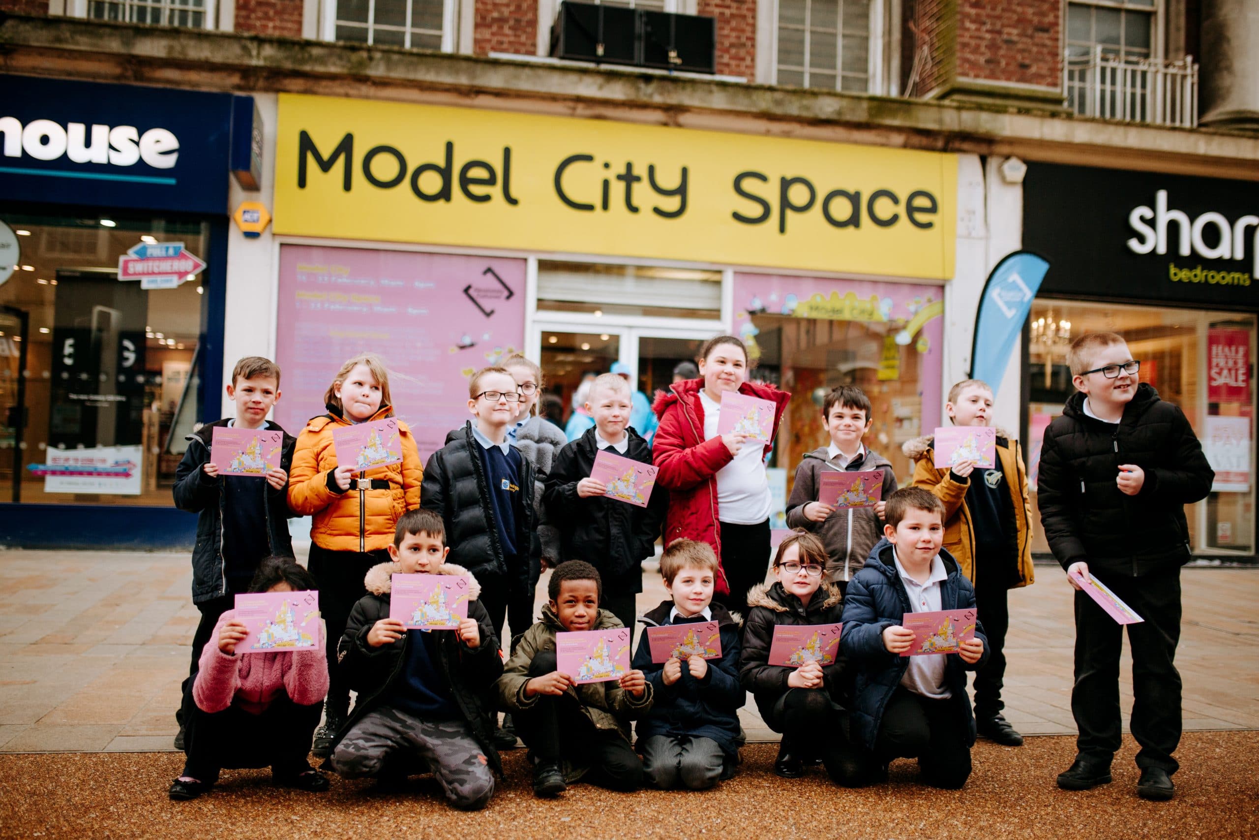 A group of children stood outside shops in Hull holding up pictures of artwork.