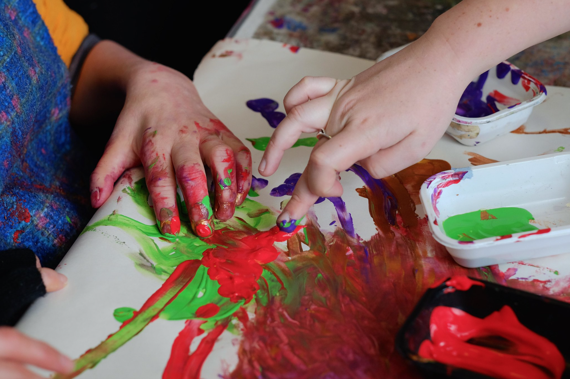 Two hands are creating artwork with red and green paints.