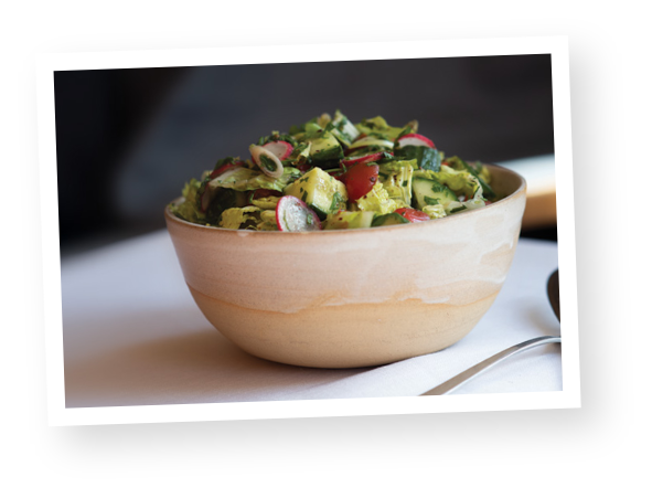 A bowl of fresh salad in a light brown bowl.