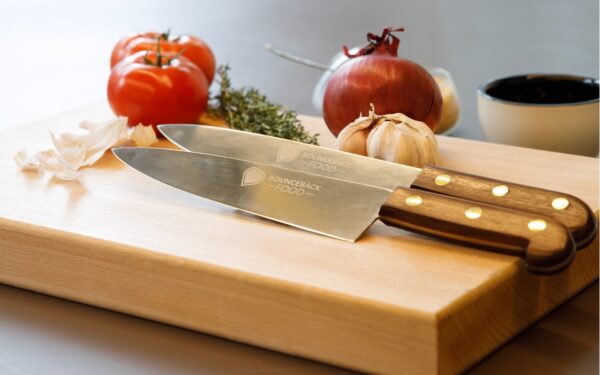 A Bounceback chef's knife placed on top of a chopping board with vegetables in the background.