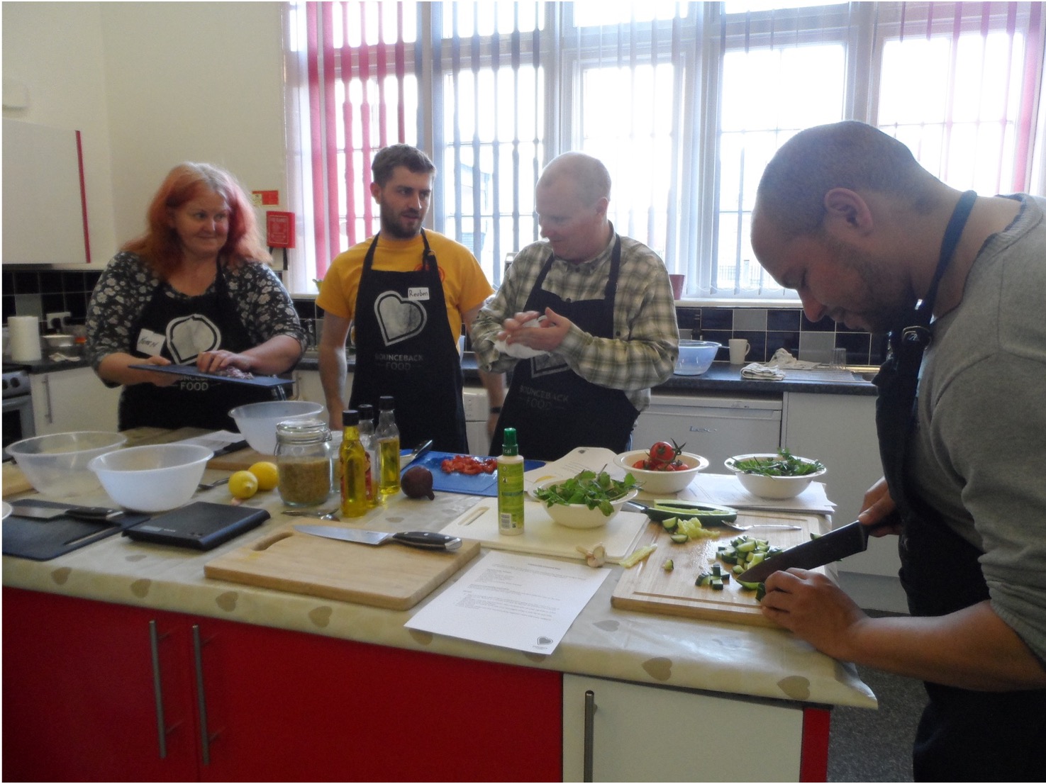 A Community Cookery School workshop is taking place around a prep table in the centre of the kitchen